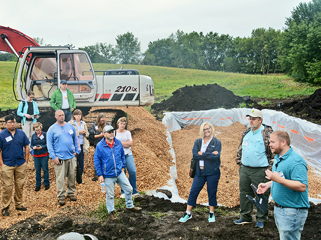 Keegan Kult, far right, executive director of the Ag Drainage Management Coalition, explains to Conservation in Action tour participants how woodchip-filled bioreactors, like this one on the Bill and Nancy Couser farm near Nevada, Iowa, remove harmful nitrates from tile drainage water before it leaves the property. (Progressive Farmer image by Matthew Wilde)